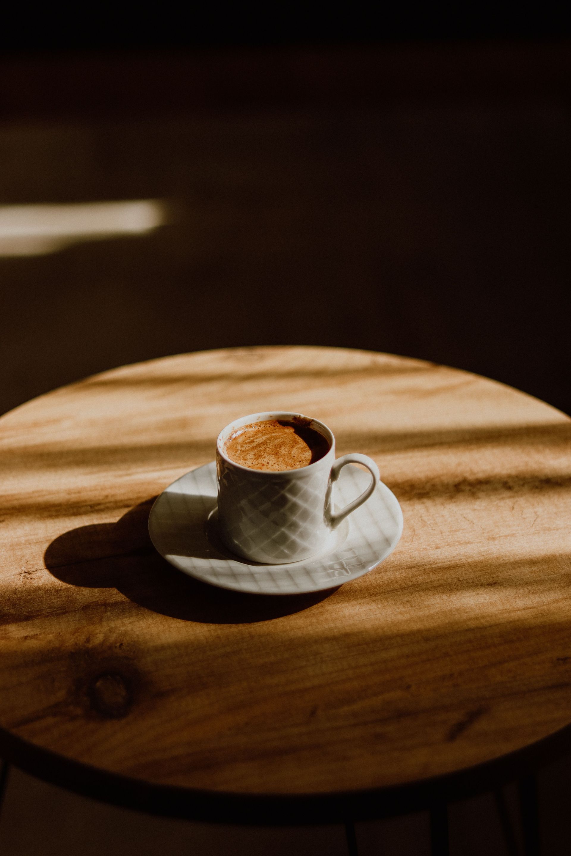 A white coffee cup with rich espresso on a sunlit wooden table creating warm contrasts.